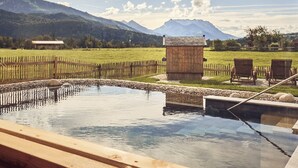 A wooden spa area with a pool, wooden benches, and a view of mountains. - Appartement Alpstyle Family (Reit im Winkl)