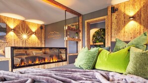 A modern bedroom with a fireplace, wooden wall paneling, and green pillows. - Appartement Alpstyle Family (Reit im Winkl)