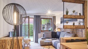 A modern living room with a wooden floor, a round wooden coffee table, a sofa with cushions, a wooden dining table, and a hanging light fixture. - Appartement Alpstyle Family (Reit im Winkl)