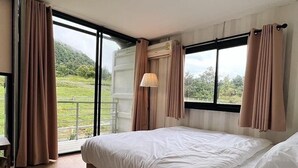 A bedroom with a large bed, a window with curtains, and a view of greenery outside. - Skugga Farm Cabin (Mae On)