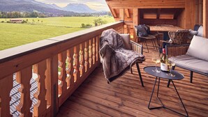 A wooden deck with a view of a green field and mountains. There are wicker chairs and a sofa with a blanket. - Appartement Alpstyle Heaven (Reit im Winkl)