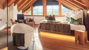 A spacious attic bedroom with a large bed, a bathtub, and a view of the mountains. - Appartement Alpstyle Heaven (Reit im Winkl)
