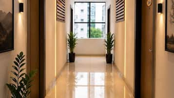 A hotel corridor with a polished floor, potted plants, and doors with a number plate.