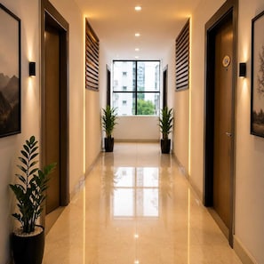 A hotel corridor with a polished floor, potted plants, and doors with a number plate.