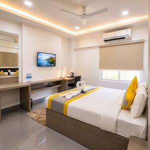 Una habitación de hotel con cama, escritorio, silla, televisor, aire acondicionado y ventana.