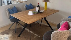 A modern kitchen with white cabinets, a dining area with a wooden table, and a painting of a coastal scene.
