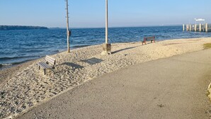 A pebbled beach with a wooden bench and two tall street lamps.
