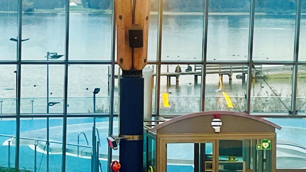 A view through large windows of a swimming pool area with a lifeguard station and a dock with boats.