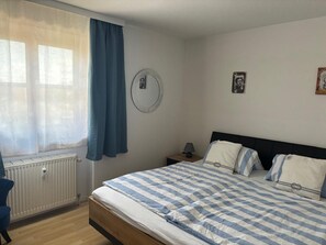 Una camera da letto con un letto, un comodino, una lampada, un termosifone e una finestra con tende.