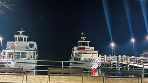 A nighttime marina with two boats docked, a wooden bench, and a metal railing.