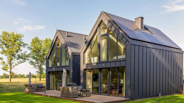 Ein modernes Haus mit großen Fenstern, einer Terrasse und Solaranlagen.