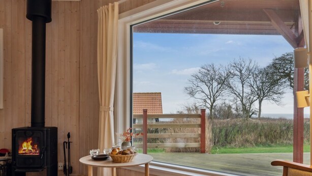 A cozy room with a wood-burning stove, a table with a basket of bread, and a view of the outdoors through a large window. - "Marlies" - 300m from the sea by Interhome (Allinge)