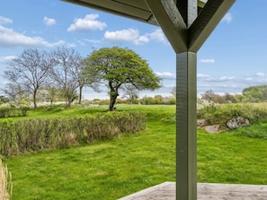 A covered outdoor area with a view of a grassy field and trees.