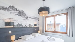 Une chambre d’hôtel moderne avec une fresque représentant une montagne, un grand lit, des lampes de chevet et une vue sur les bâtiments par la fenêtre.
