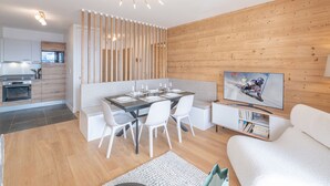 Un salon moderne avec un coin repas, des murs en bois, un téléviseur et une cuisine à l’arrière-plan.