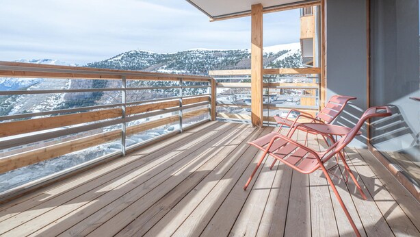 Une terrasse en bois offrant une vue sur des collines enneigées et un ciel dégagé.