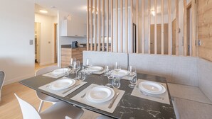 Un espace repas moderne avec une table en verre pour six personnes, un séparateur en bois et une cuisine en arrière-plan.