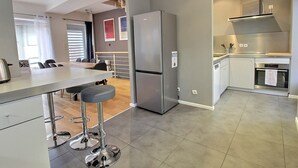 A modern kitchen with a stainless steel refrigerator, a bar area with stools, and a dining table. - Elegant Home in Colmar: Terrace, Hot Tub, Parking, Steps from Historic Center (Colmar)