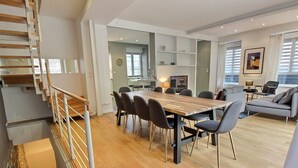 A spacious living area with a wooden dining table, grey sofas, and a staircase. - Elegant Home in Colmar: Terrace, Hot Tub, Parking, Steps from Historic Center (Colmar)