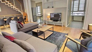 A modern living room with a sofa, coffee table, and TV. There is a staircase leading to another level. - Elegant Home in Colmar: Terrace, Hot Tub, Parking, Steps from Historic Center (Colmar)