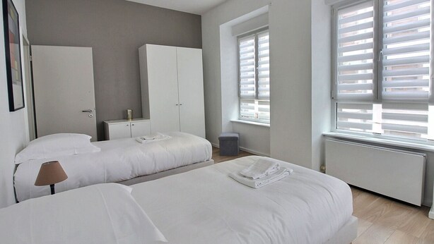 A bedroom with two beds, a wardrobe, a radiator, and a window with blinds. - Elegant Home in Colmar: Terrace, Hot Tub, Parking, Steps from Historic Center (Colmar)