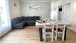 Una sala moderna con un sofá modular, una mesa de comedor con sillas, un cuadro en la pared y una lámpara en el techo.