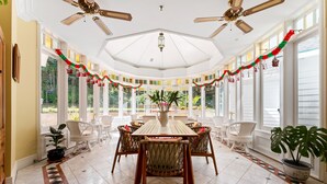 Una sala de estar con ventanales, una mesa grande y sillas, decorada con guirnaldas festivas.