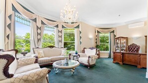Un salón espacioso con una gran lámpara de araña, muebles elegantes y ventanas amplias que dan a zonas verdes.