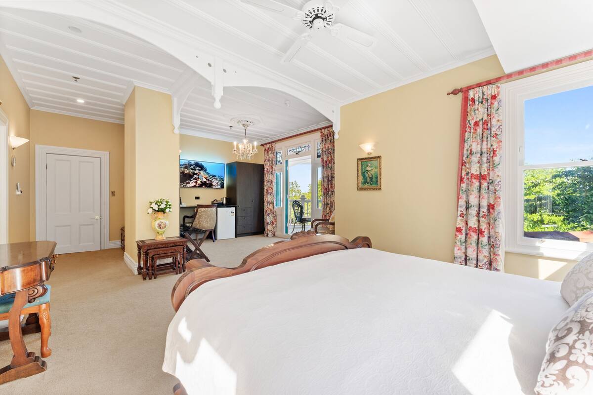 A spacious bedroom with a large bed, a desk, and a view of greenery outside.