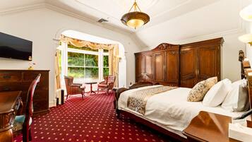 A hotel room with a large bed, a wooden wardrobe, a desk with a chair, a television, and a window with curtains.