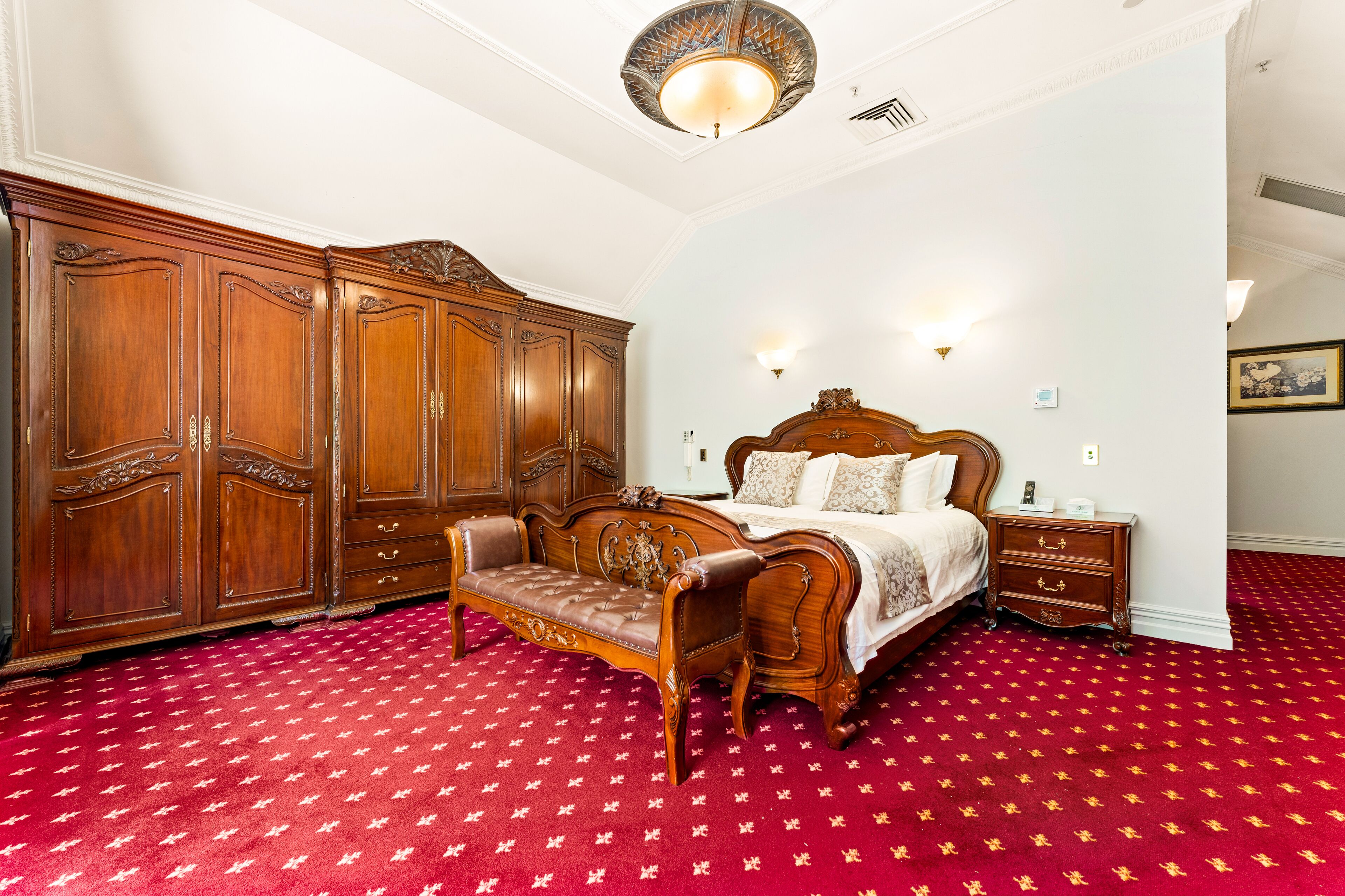 Une chambre à coucher avec une grande armoire en bois, un lit en bois doté d’une tête de lit et un tapis rouge à motifs.