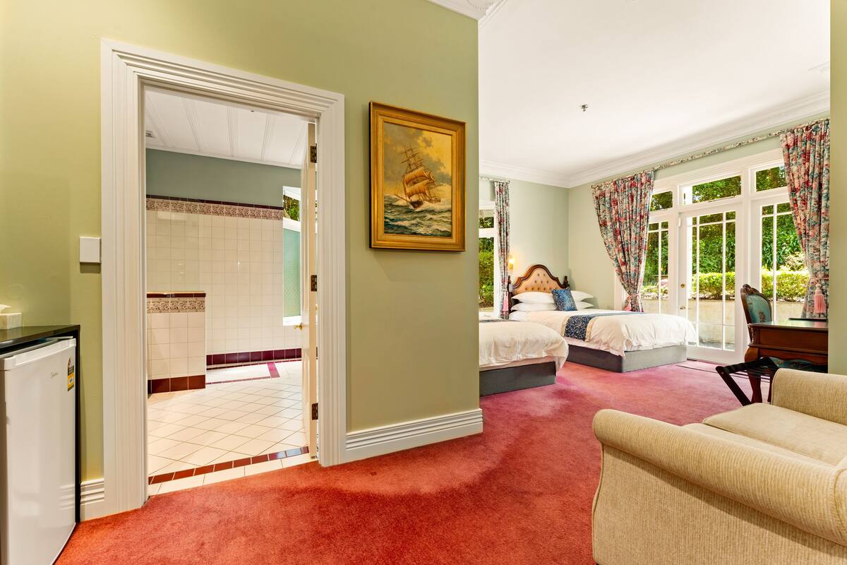 A bedroom with a bed, a painting, a desk, and a window with curtains.