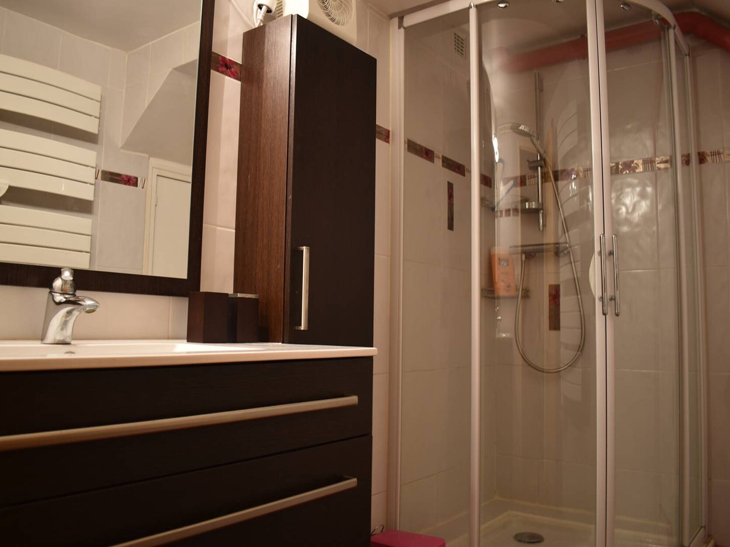 A modern bathroom with a glass-enclosed shower, a dark wooden cabinet, and a white sink with a chrome faucet.
