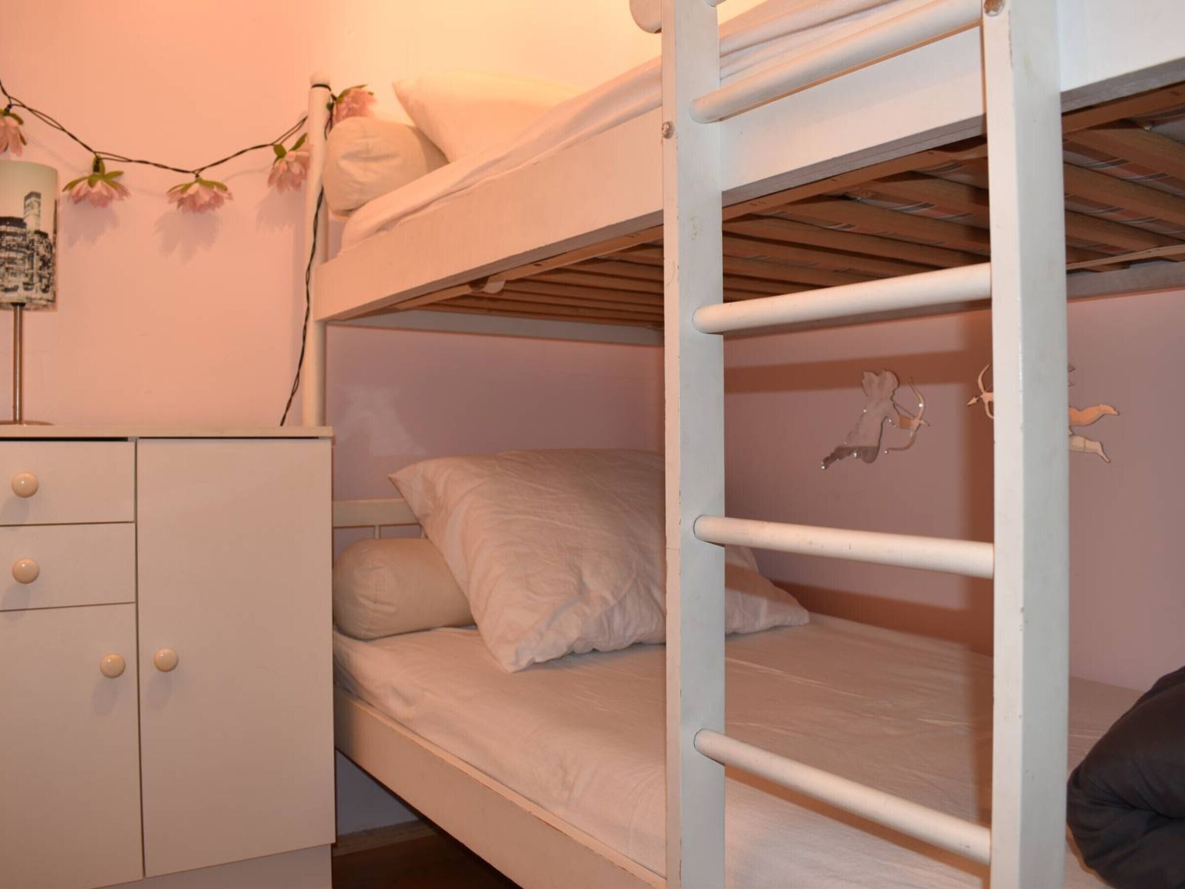 A bunk bed with white bedding and a small dresser with drawers.
