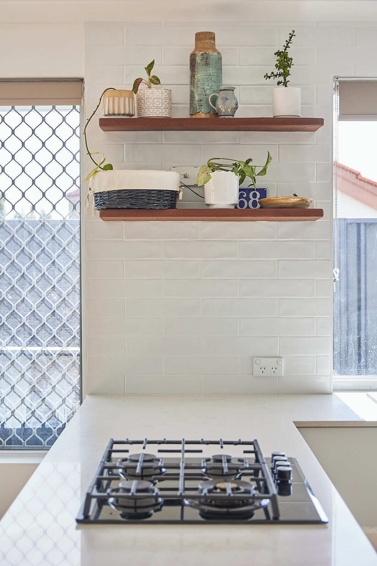 A kitchen with a gas stove, white tiled walls, and shelves with decorative items.
