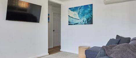 A living room with a flat-screen TV, a large abstract painting, a grey sofa, and a small wooden side table.