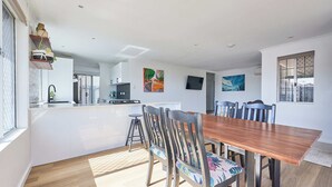 A modern kitchen with white cabinets, a black faucet, and a small island. There is a dining area with a wooden table and chairs, and a TV mounted on the wall. - Sunny Scarborough Stay-Freshly Renovated! (Scarborough)