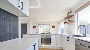 A modern kitchen with white cabinetry, a stainless steel oven, and a large window providing natural light. - Sunny Scarborough Stay-Freshly Renovated! (Scarborough)