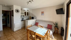 Un espace de vie compact comprenant un coin repas, une kitchenette et un canapé avec un téléviseur.