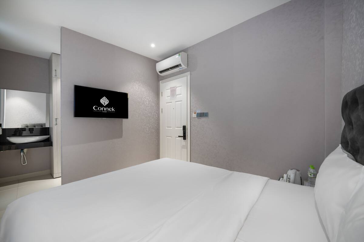 Une chambre d’hôtel équipée d’un lit, d’un téléviseur fixé au mur, d’une salle de bain avec un lavabo et un miroir, et d’un appareil de climatisation.