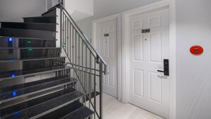 A staircase with black steps and metal railings leading to a white door with a number plate.
