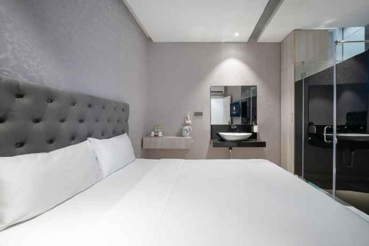 Une chambre à coucher moderne avec une tête de lit capitonnée, un grand lit, une table de chevet avec une lampe et une cabine de douche en verre.