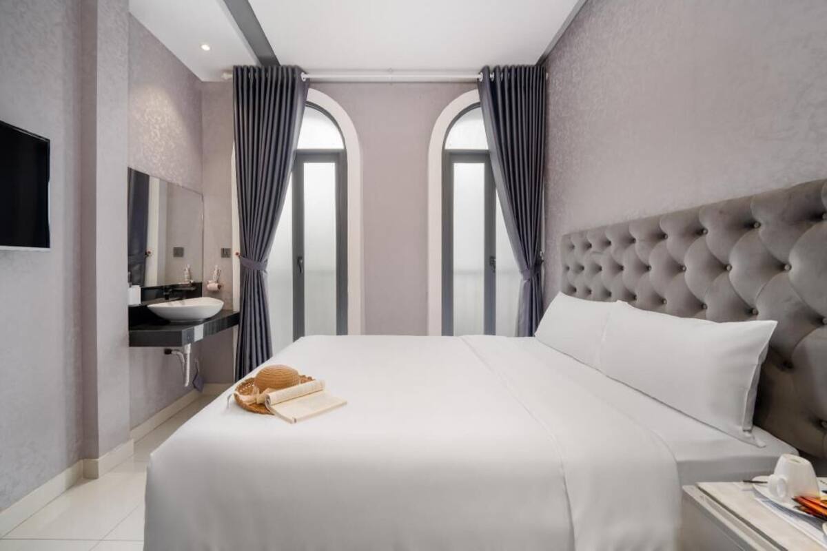 Une chambre d’hôtel moderne dotée d’un grand lit, d’une table de chevet, d’une coiffeuse intégrée avec un miroir et de deux fenêtres avec des rideaux.