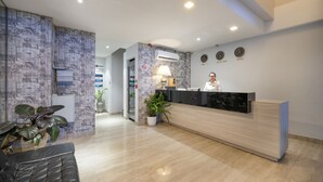 A hotel reception area with a modern design, featuring a reception desk, a waiting area with a sofa, and potted plants.