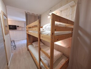 Ein Schlafraum mit Etagenbetten, einem Fernseher an der Wand, Holzboden und einem Vorhang.