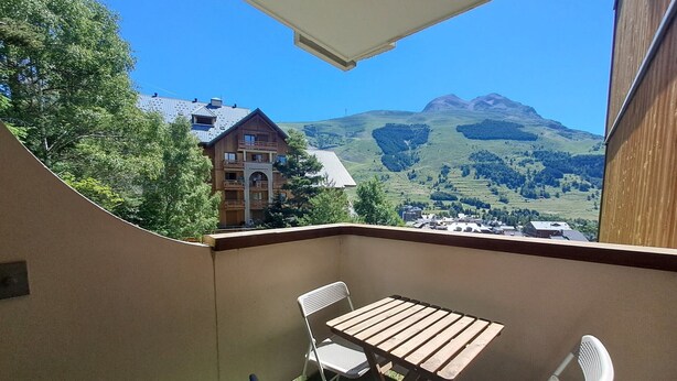 A balcony with a table and chairs, overlooking a mountainous landscape and a building with a balcony. - Cozy studio 3 ppl, pets ok, parking - Les Deux Alpes (Les Deux Alpes)