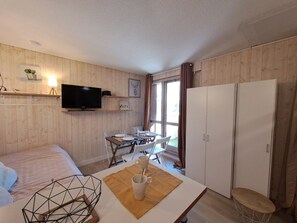 Ein Zimmer mit Holzwandverkleidung, einem Bett, einem an der Wand montierten Fernseher, einem Esstisch mit Stühlen und einem Kleiderschrank.