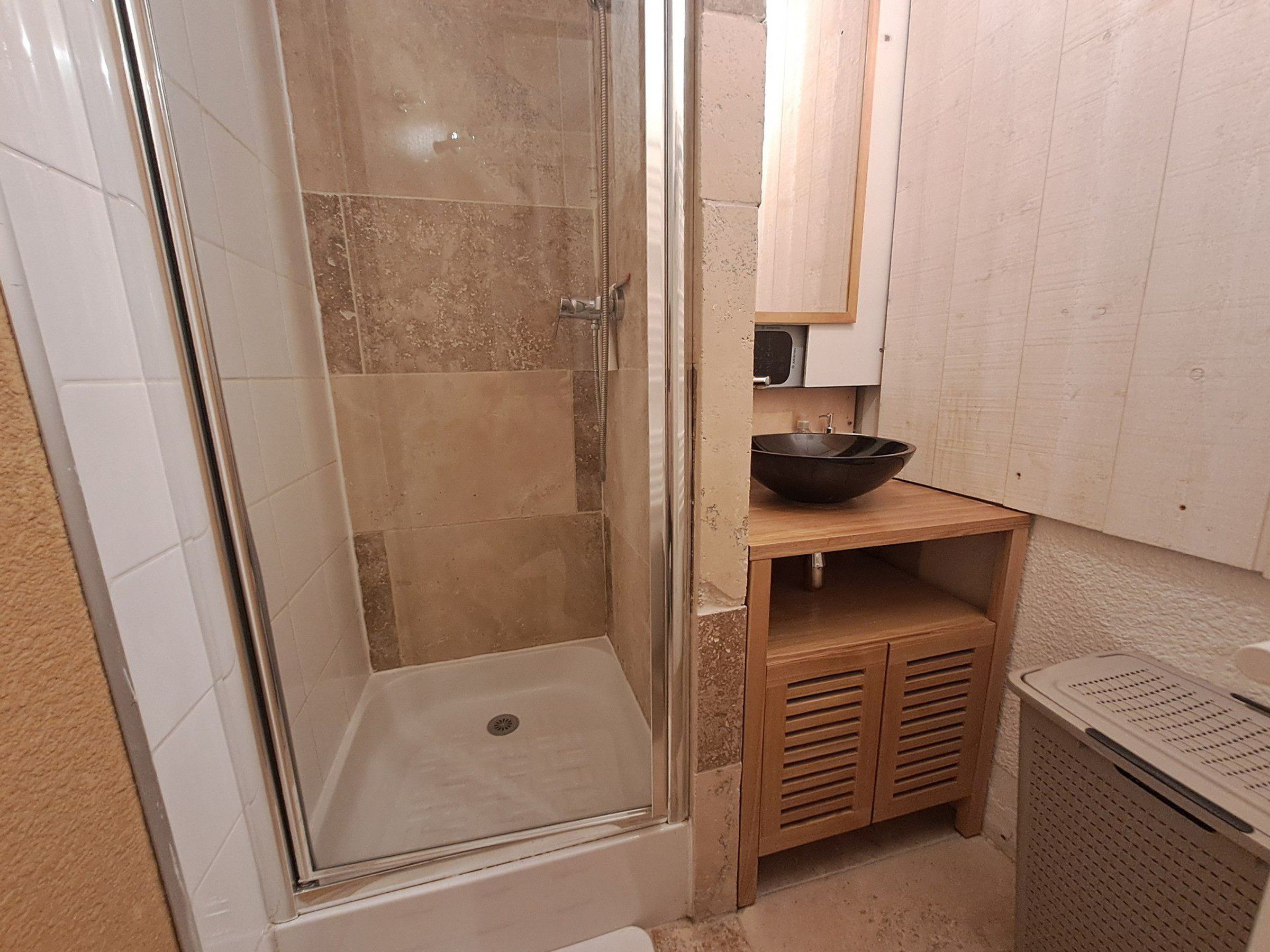 A shower with a glass door, a sink with a bowl, and a laundry basket.