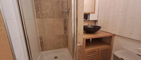 A shower with a glass door, a sink with a bowl, and a laundry basket.