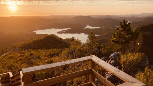 Eine Holzterrasse mit Blick auf ein Tal, einen See und ferne Berge.